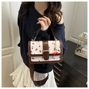 Small crossbody bag with cute cherry print and brown leather trim held by model.