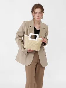Hand-held stylish straw woven tote bag with white trim displayed by a fashion model.