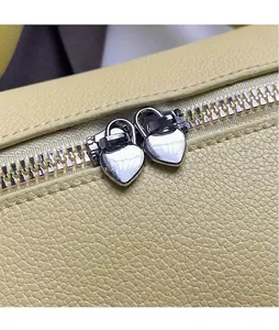 Detailansicht einer gelben Handtasche mit silbernen herzförmigen Metall-Reißverschlüssen