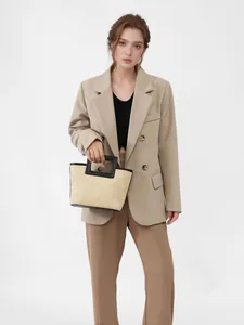 Woven straw handbag with black square handle held by a model in a beige blazer