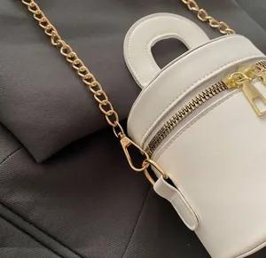 Detaillierte Ansicht der goldenen Kette und des Doppelreißverschlusses der weißen Tasche.