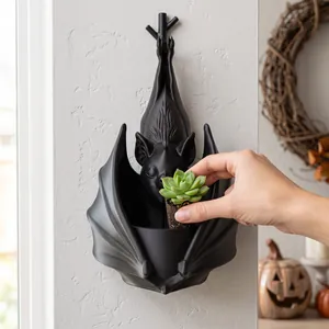 Gros plan d'une main plaçant une succulente dans un pot mural chauve-souris gothique.