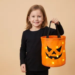 Close-up of a child holding a glowing LED pumpkin candy bucket for Halloween