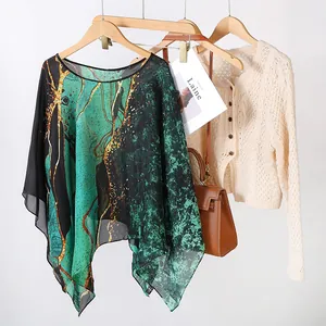 Détail d'un poncho en mousseline à imprimé abstrait vert sur un cintre en bois.