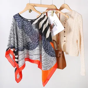 Présentation stylisée d'un poncho en soie imprimé avec des motifs de plumes.