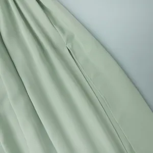 Gros plan sur l'élégante fente latérale et la texture plissée d'une jupe longue vert sauge.