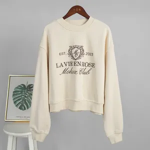 Close-up of a cream crew neck sweatshirt featuring vintage-style chest embroidery