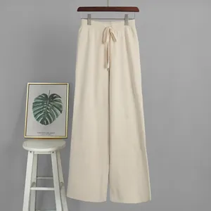 Beige knitted wide-leg pants with drawstring waist hanging on minimalist gray background