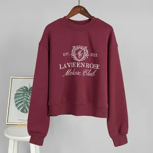 Close-up of a burgundy crewneck sweatshirt with 'La Vie En Rose' embroidery on the chest.