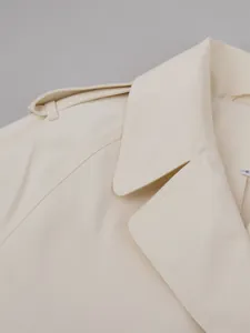 Detail showing the lapel collar and fine shoulder stitching on a cream trench coat.