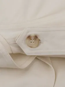 Detailed close-up of marble-pattern button and precision stitching on beige trench coat