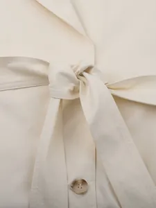 Close-up of tied waist belt on cream-colored stylish long trench coat with button detail.