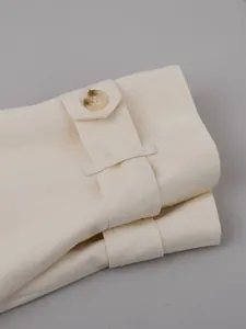 Detailed view of cream-colored trench coat cuff with decorative button and strap