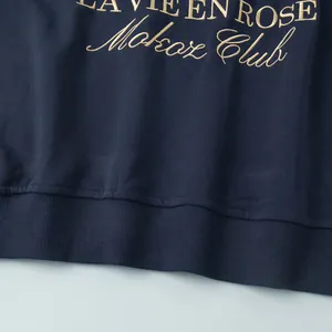 Detailed macro view of gold "La Vie En Rose" embroidery on a navy blue sweatshirt.