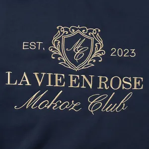 Close-up of golden embroidery detail on navy sweatshirt featuring Mokoz Club crest