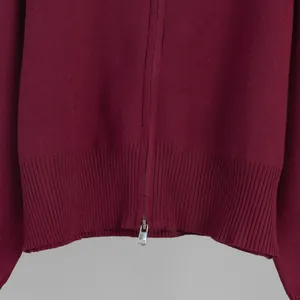 Close-up detail of maroon knitted sweater with metal zipper and ribbed hem texture.