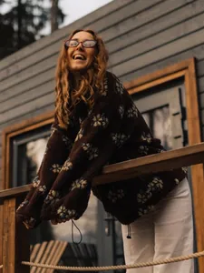Close-up of woman in brown floral fleece hoodie on a rustic wooden balcony during winter