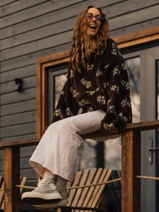 Outdoor lifestyle shot of a woman wearing a warm brown floral fleece hoodie and white pants.
