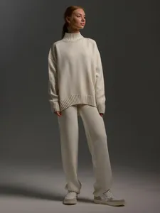 Detail of women's cream mock neck sweater and knit trousers set for a cozy autumn look.