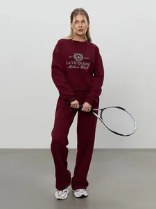 Close-up of burgundy embroidered sweatshirt and pants set held with tennis racket