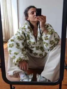 Close-up detail of a white fleece quarter-zip sweatshirt with green flower prints on a model