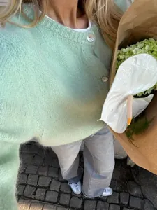 Detailaufnahme einer mintgrünen Strickjacke mit weißen Knöpfen und weicher Textur.