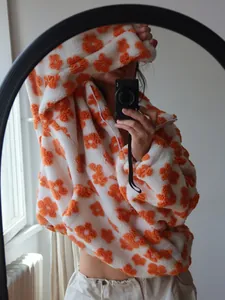 A detailed lifestyle view of a cozy white fleece hoodie with vibrant orange flower patterns