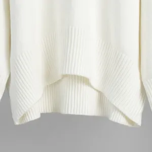 Primo piano di un maglione bianco in maglia con bordo a coste morbido e design ricurvo.
