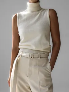 A close-up detail of a minimalist cream sleeveless turtleneck knit vest and trousers