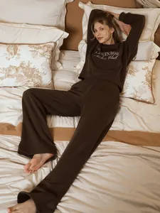 Elegant dark brown two-piece loungewear set with white embroidered text on soft bedding.