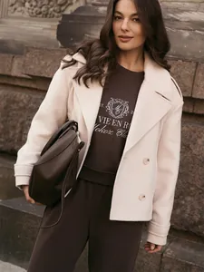Model wearing a dark brown embroidered sweatshirt and pants set with a stylish cream coat