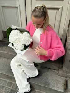 Frau in einem leuchtend rosa flauschigen Strickcardigan mit weißen Hortensien draußen