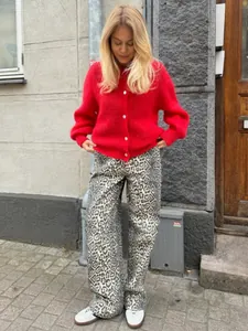 Model trägt eine leuchtend rote Strickjacke mit Knöpfen in einer schicken städtischen Umgebung.