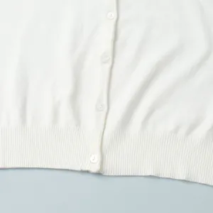 Detailed macro view of the white knitted cardigan featuring buttons and ribbed hem