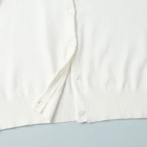 Close-up of white knitted cardigan with elegant buttons and ribbed hem texture.