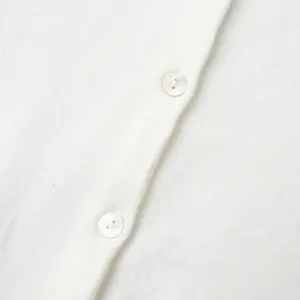 Detailed close-up showing the soft texture and pearl buttons of a white knitted cardigan