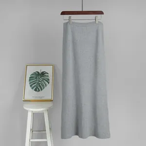 Detail view of a gray knitted midi skirt hanging on a wooden hanger against gray wall