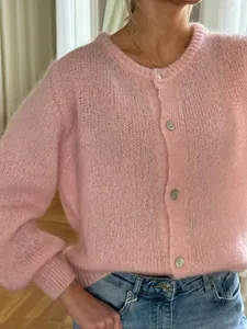 Detailaufnahme der weichen Textur und der einreihigen Knöpfe einer rosa Strickjacke