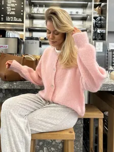 Weiche rosa Strickjacke mit Knöpfen in einer gemütlichen Café-Atmosphäre.