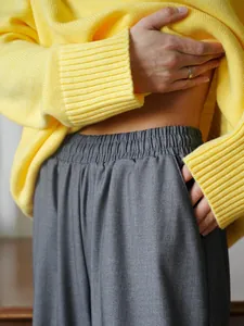 Dettaglio ravvicinato di un maglione giallo in maglia e pantaloni larghi grigi.