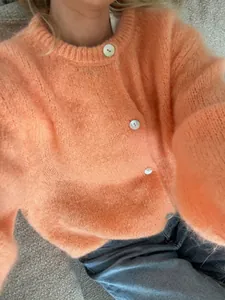 Detailaufnahme einer flauschigen pfirsichfarbenen Strickjacke mit weißen Knöpfen