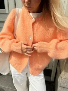 Detailansicht eines flauschigen pfirsichfarbenen Strickcardigans mit weißen Knöpfen im Freien