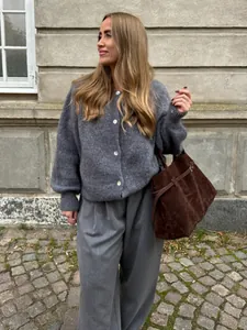 Stilvolles Modell trägt eine graue Strickjacke mit einer braunen Wildledertasche im Freien