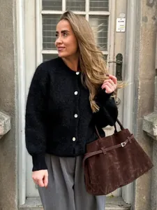 Elegante Frau in einer schwarzen flauschigen Strickjacke mit weißen Knöpfen im Freien