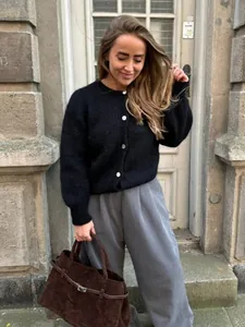 Frau trägt eine schwarze Strickjacke mit weißen Knöpfen in einer stilvollen Umgebung.