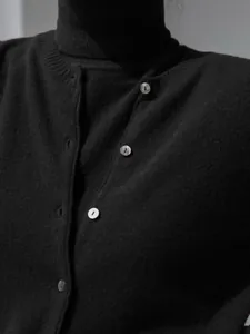 Close-up detail of black knit cardigan featuring iridescent shell buttons and turtleneck.