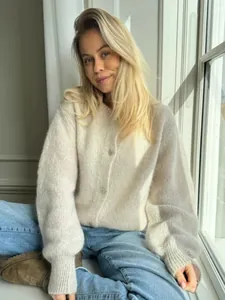 Modell trägt eine gemütliche cremefarbene Strickjacke mit Knöpfen und sitzt am Fenster