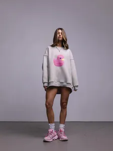 Vista dettagliata di una felpa grigia oversize con stampa anatra rosa su una modella donna