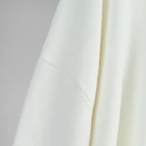 Detailed close-up showing the soft white knitted sweater shoulder seam and fine ribbed texture