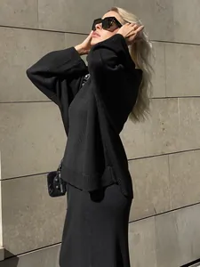 Full body view of a woman wearing a chic black knit sweater and long skirt set